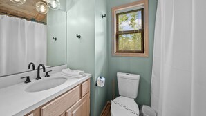 Baño con lavabo, espejo, inodoro y ventana con persianas.