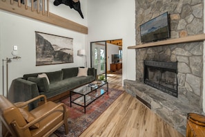 A living room with a stone fireplace, a sofa, a coffee table, and a television mounted on the wall.