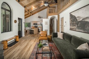 A spacious living area with a high ceiling, wooden beams, a green sofa, a coffee table, and a painting on the wall.