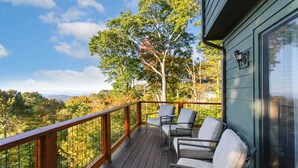 Terraza de madera con mobiliario exterior, con vista a un paisaje boscoso.