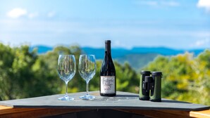Una mesa con una botella de vino, dos copas y unos prismáticos frente a un paisaje pintoresco.