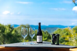 Un tavolo con una bottiglia di vino, due bicchieri e binocoli, con una vista panoramica sullo sfondo.