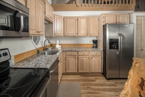 A kitchen with wooden cabinets, a stainless steel refrigerator, a microwave, and a stove.