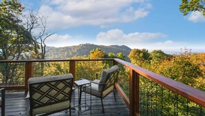 Terraza de madera con dos sillas y una pequeña mesa, con vistas a una ladera boscosa.