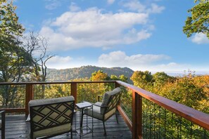 Un terrazzo in legno con due sedie e un tavolino, vista su un pendio boscoso.