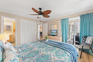 A hotel room with a bed, a television, a ceiling fan, and a view of the outdoors.