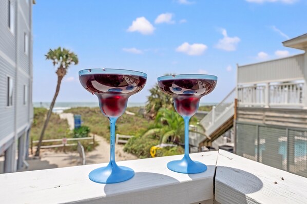 Two glasses of red wine on a white railing with a view of a beach and buildings in the background.