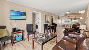A living room with a TV, a coffee table, a sofa, and a dining area with chairs and a table.