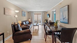 A living room with a leather sofa, a dining table with chairs, a TV, and artwork on the walls.