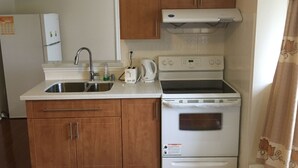 Une cuisine de taille réduite, dotée de meubles en bois, d’un évier en acier inoxydable, d’une cuisinière blanche et d’un réfrigérateur.
