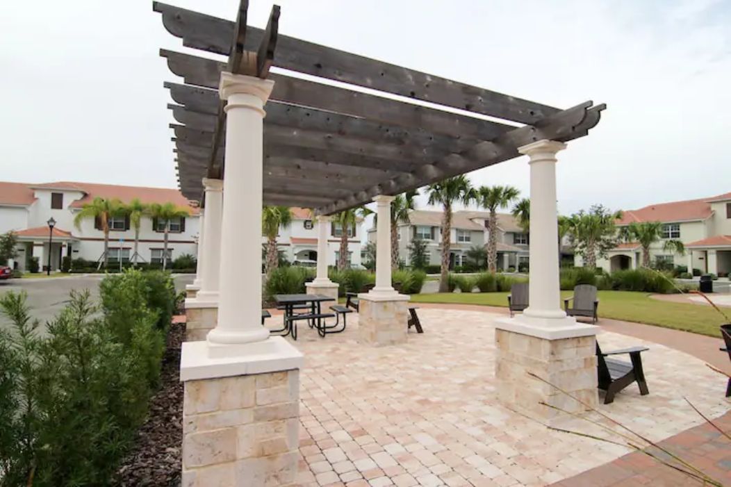 Un patio couvert agrémenté de colonnes en pierre et d’une pergola, avec des sièges d’extérieur et une vue sur les immeubles résidentiels en arrière-plan.