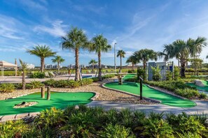 A miniature golf course with green putting greens, palm trees, and a clear blue sky.