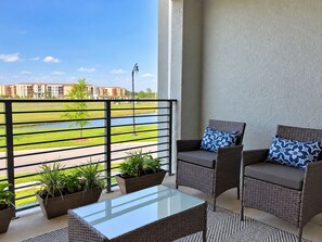 A balcony with wicker furniture, a glass table, and potted plants. - Sophisticated Condo, up to 6, Only 7 min to Disney (Kissimmee)
