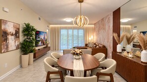 A modern dining area with a round table, chairs, and a TV mounted on the wall. - Sophisticated Holiday Condo, Only 7 min to Disney (Kissimmee)
