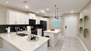 A modern kitchen with white cabinetry, stainless steel appliances, and a central island. - Sophisticated Holiday Condo, Only 7 min to Disney (Kissimmee)