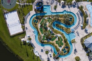 An aerial view of a resort with a large swimming pool, a water slide, and a beach area.