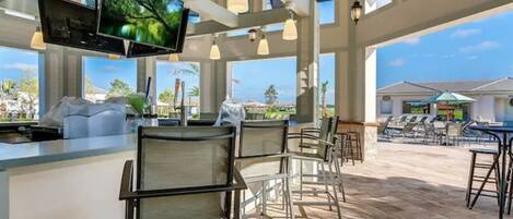 A bar area with a TV screen, outdoor seating, and a view of the ocean.