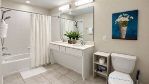 Une salle de bain avec une baignoire, une douche, un lavabo, des toilettes et un tableau représentant des fleurs au mur.