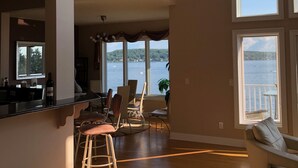 A spacious living area with a kitchen, dining area, and large windows overlooking a body of water. - Beautiful Saratoga Lake waterfront Townhouse + Community Amenities (Saratoga Springs)