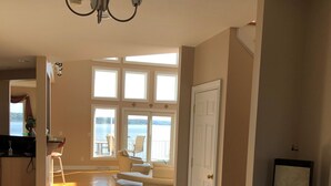 A spacious living area with a large window, a white sofa, and a chandelier. - Beautiful Saratoga Lake waterfront Townhouse + Community Amenities (Saratoga Springs)