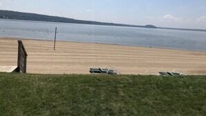 A beach with a volleyball net, a grassy area, and a view of the water. - Beautiful Saratoga Lake waterfront Townhouse + Community Amenities (Saratoga Springs)