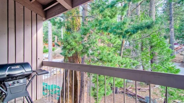 A covered outdoor area with a grill, wooden railing, and a view of pine trees. - (A203) Loft Condominiums (Yosemite National Park)