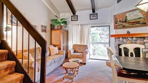 A cozy living room with a staircase, a sofa, a chair, a small table, and a stone fireplace. - (A203) Loft Condominiums (Yosemite National Park)