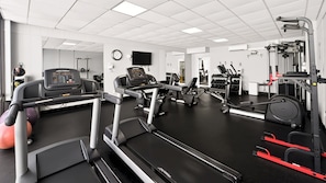Une salle de sport équipée de tapis de course, d’appareils de musculation et de ballons d’exercice.