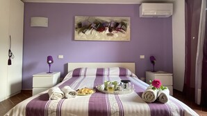 Una cama bien hecha con una colcha a rayas morada y blanca, una bandeja con alimentos para el desayuno y un cuadro en la pared.