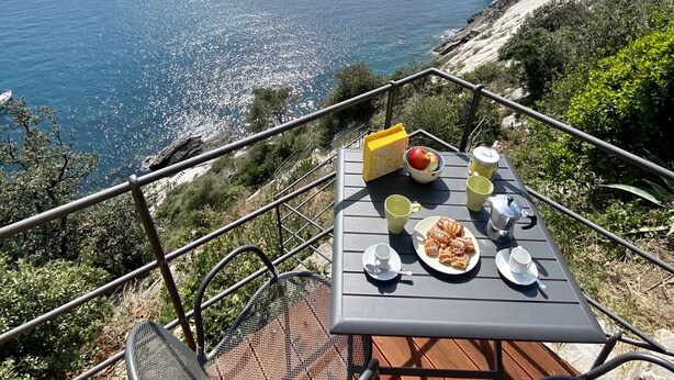 Una mesa con alimentos para el desayuno en una terraza con vista al mar.