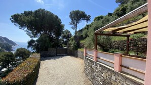 Un camino de grava que conduce a un muro de piedra con una pérgola de madera a la derecha.