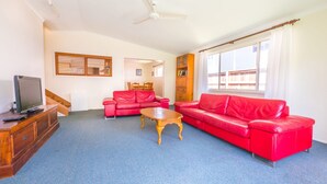 A living room with a red sofa, a wooden coffee table, and a television on a wooden cabinet. - Ngungun Street 10, Dicky Beach (DICKY BEACH)