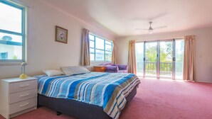 A bedroom with a bed, a nightstand, a chair, a window, and a sliding glass door leading to an outdoor area. - Ngungun Street 10, Dicky Beach (DICKY BEACH)