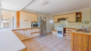 A modern kitchen with white cabinets, a refrigerator, a microwave, a stove, and a sink. - Ngungun Street 10, Dicky Beach (DICKY BEACH)