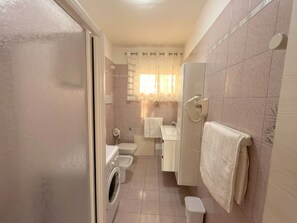 Ein kleines Badezimmer mit Waschmaschine, Toilette und Duschbereich.