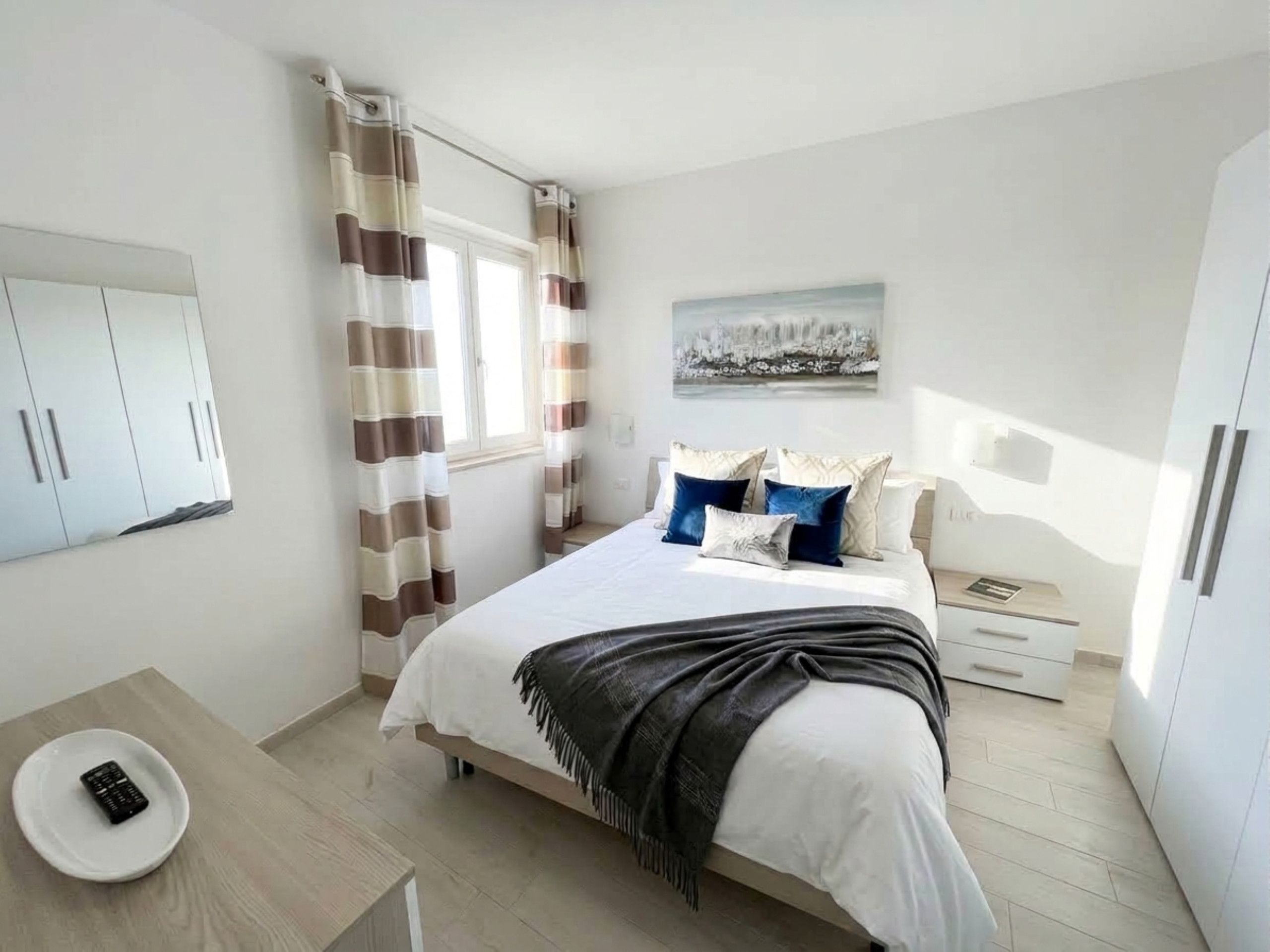 A bedroom with a bed, bedside tables, a desk, and a window with curtains.