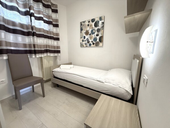 Un dormitorio pequeño y ordenado con una cama individual, una silla y una obra de arte colgada en la pared.