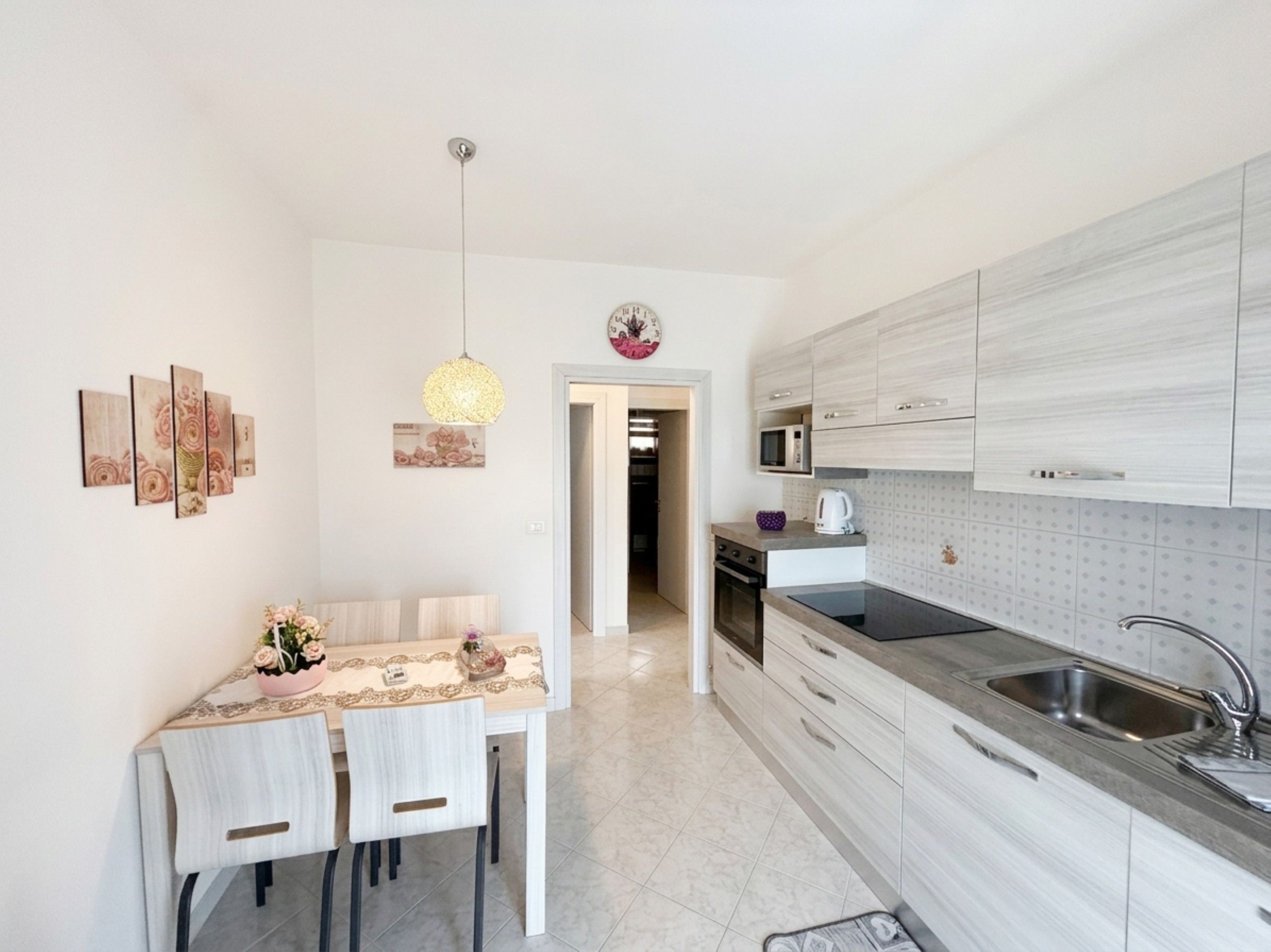 A modern kitchen with white cabinetry, a dining table with chairs, a pendant light, and a microwave.