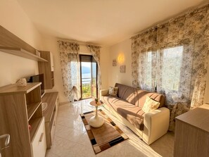 A modern living room with a sofa, a coffee table, and a view of the sea through a sliding door. - Casa Palanca Holideal (Tremosine)