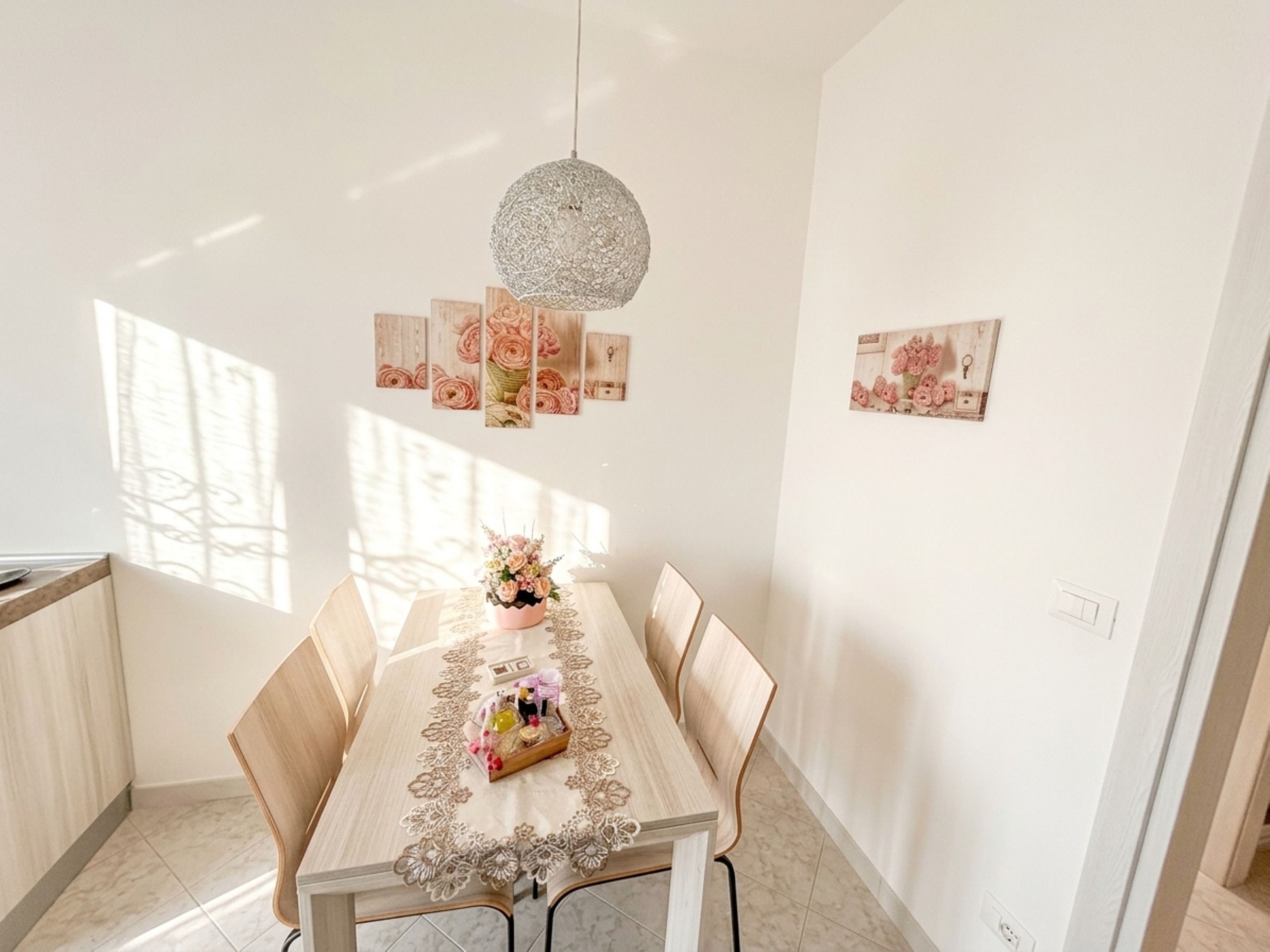Un área de comedor con una mesa lista para dos personas, una lámpara colgante y cuadros de flores en la pared.