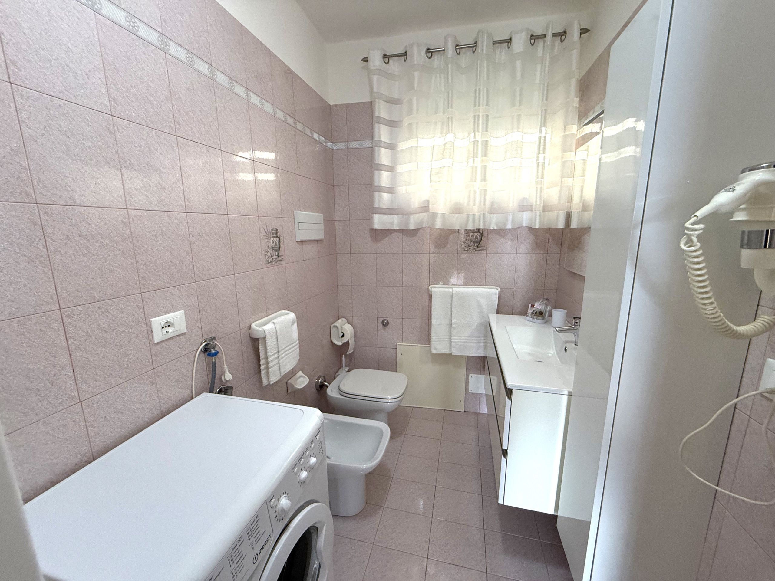 A bathroom with a washing machine, toilet, bidet, and a telephone.