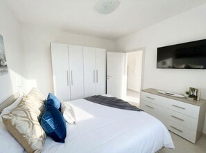 A bedroom with a bed, white wardrobe, and a TV.