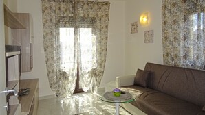 Ein Wohnzimmer mit einer Couch, einem Glastisch mit einer Blume und einer Tür mit einem gemusterten Vorhang.
