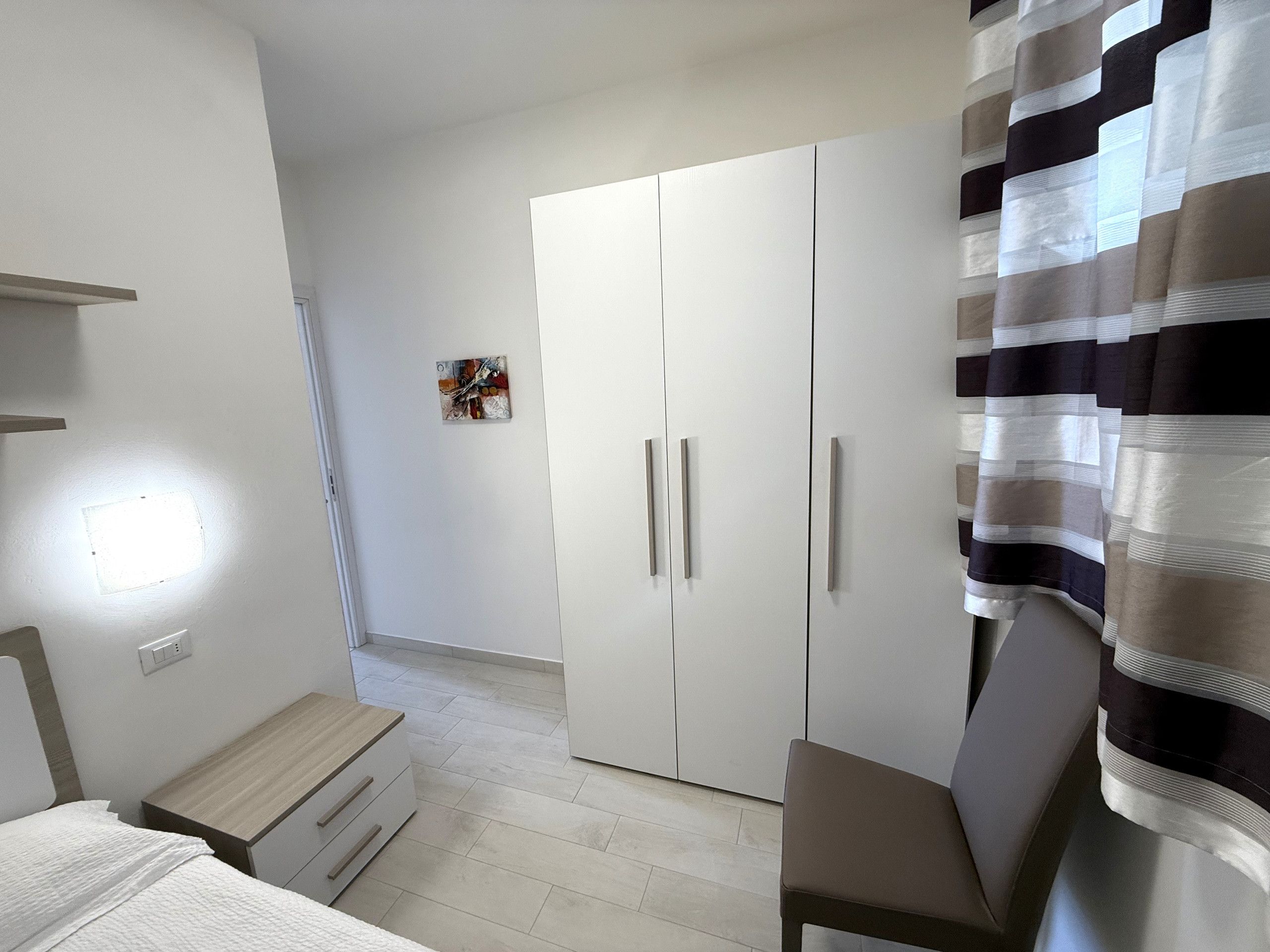 A bedroom with a bed, a bedside table, a wardrobe, and a curtain.