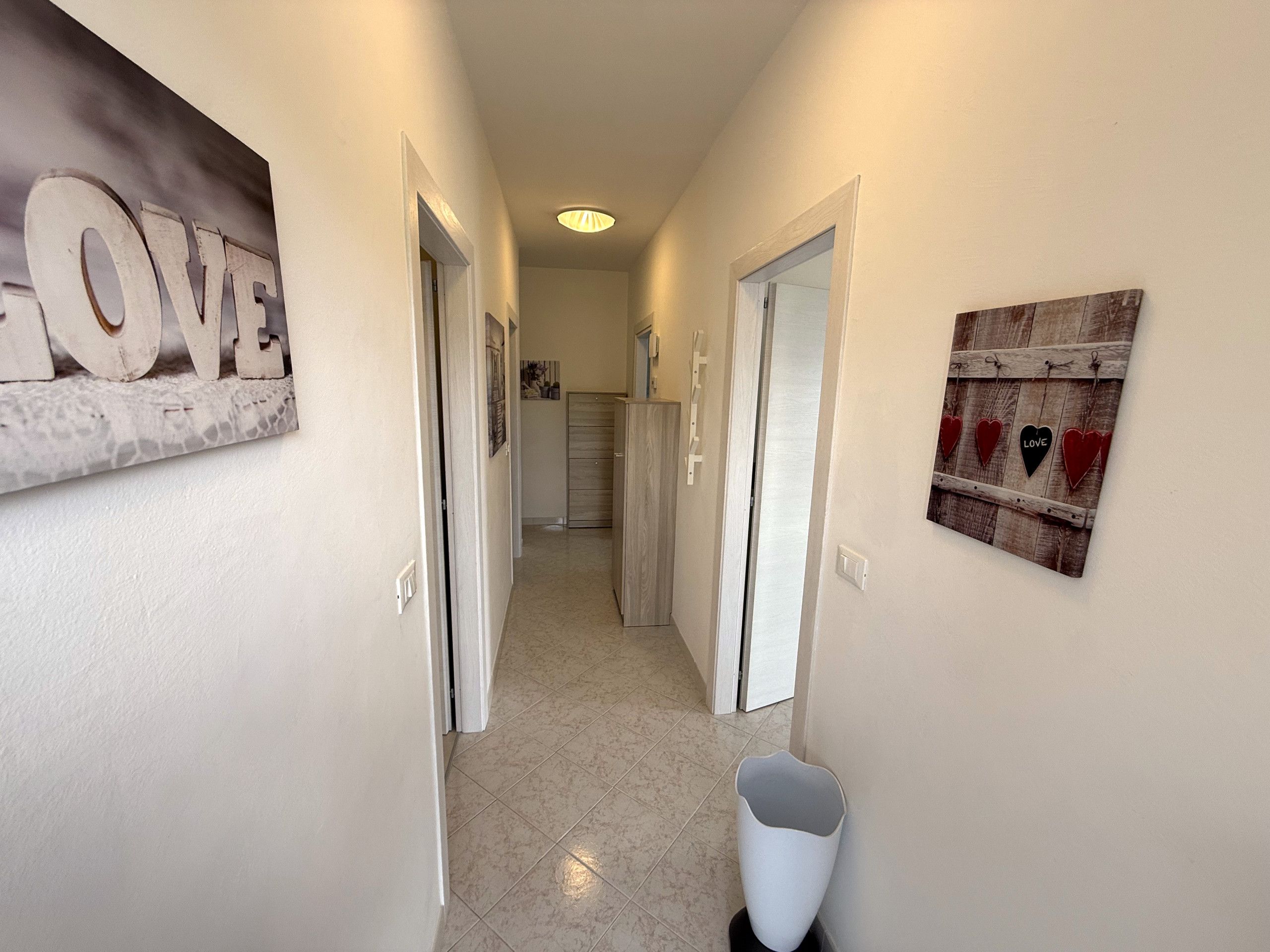 Un couloir orné d’une pancarte « LOVE », d’une enseigne en bois décorée de cœurs et d’une poubelle blanche.