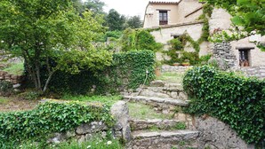 A rustic stone staircase leading to a traditional stone building with ivy-covered walls and a window with a wooden shutter.