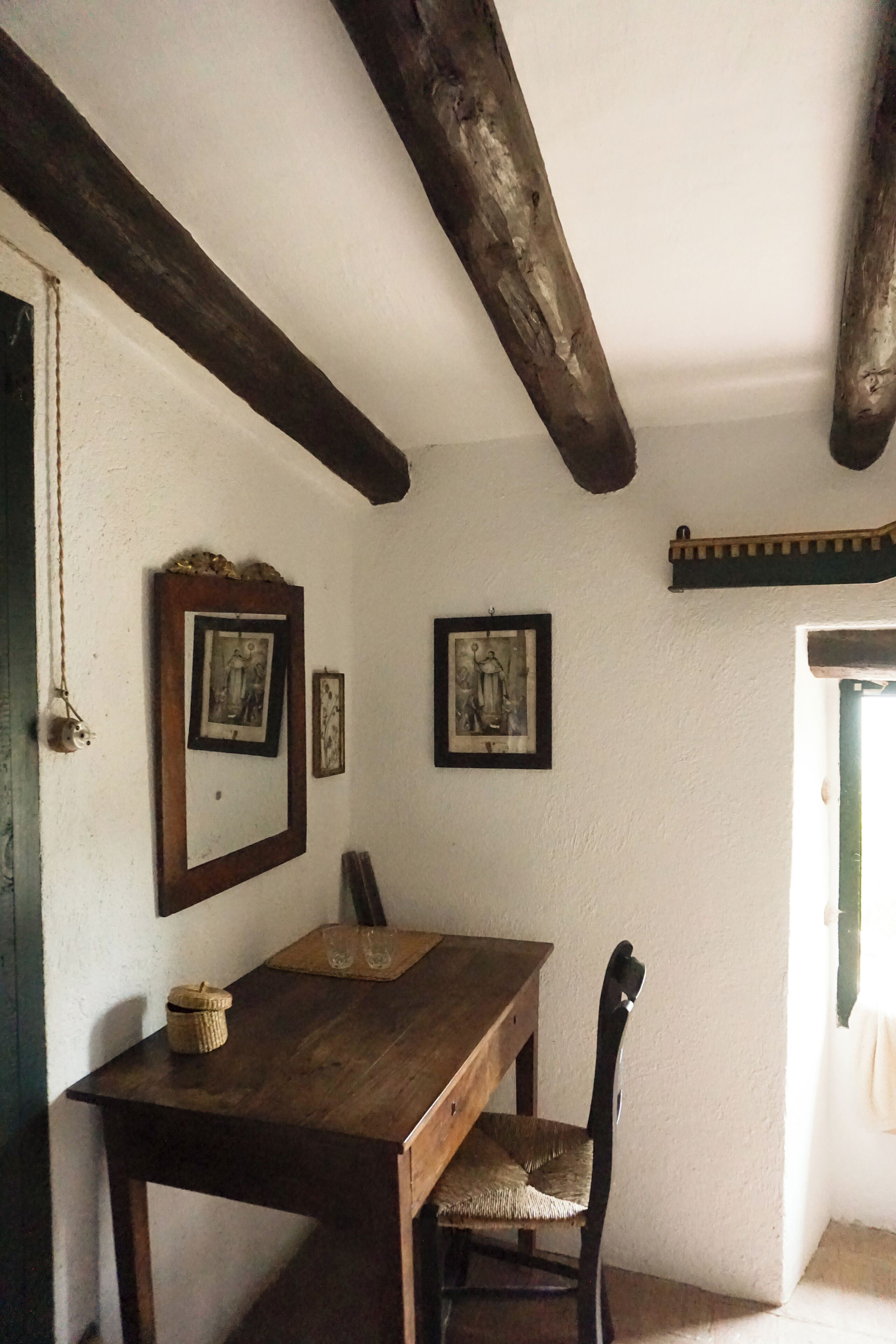 A room with a wooden table and chair, framed pictures on the wall, and exposed wooden beams.