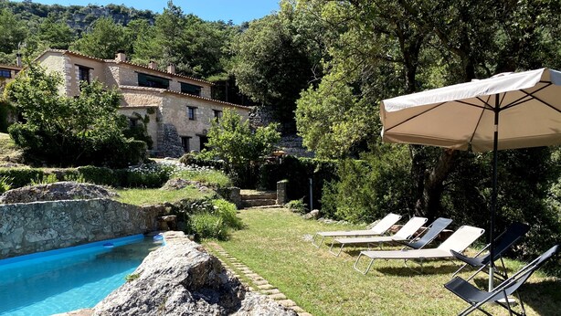 A pool area with lounge chairs and a large umbrella, surrounded by stone walls and greenery.