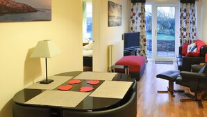 A compact living space with a dining area, a sofa, a television, and a view of the outdoors. - Dove Cottage - UK3284 (Acklington, near Amble)