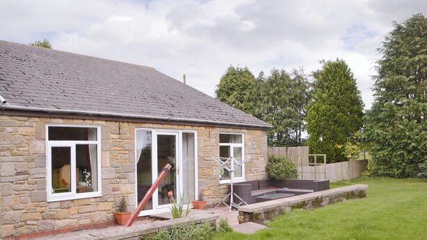 A stone house with a tiled roof, a front door, and a small garden area with grass and a wooden fence. - Dove Cottage - UK3284 (Acklington, near Amble)